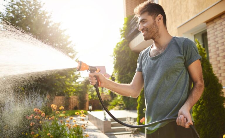 Man using garden hose with strong water pressure cleaner effect in backyard