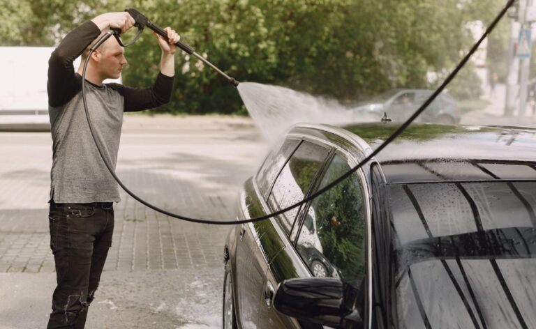Water pressure cleaner being used to rinse a black car with high-powered spray
