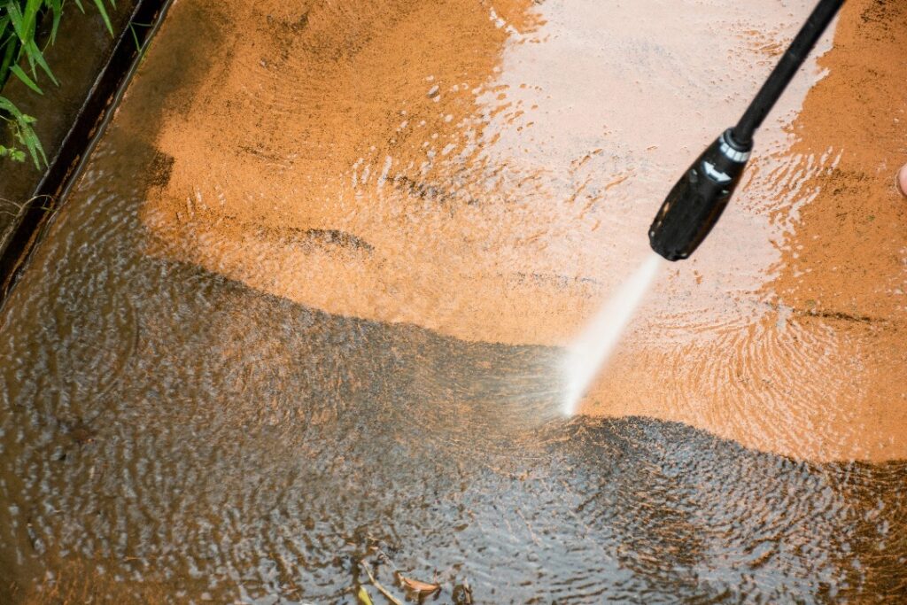 High pressure cleaner removing dirt from concrete surface with powerful water spray