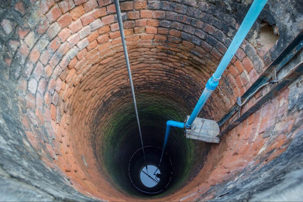 Brick-lined traditional water well with PVC pipes connected to a submersible water pump system for groundwater extraction.