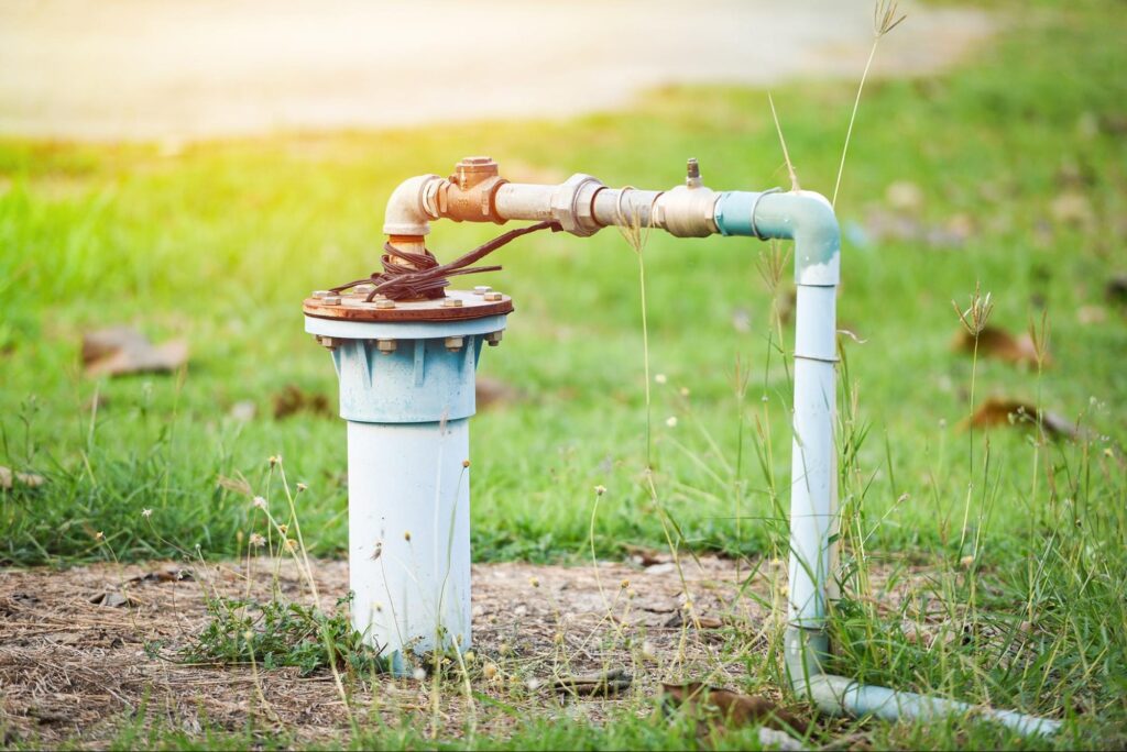 Outdoor borehole installation with PVC piping and valve connected to a submersible water pump for clean water supply.