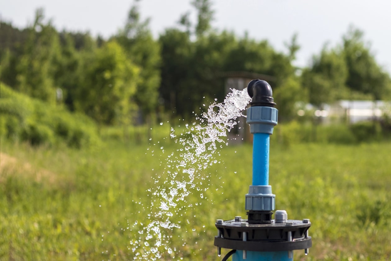 Blue PVC pipe pumping groundwater with strong water flow from a submersible water pump for agricultural irrigation.