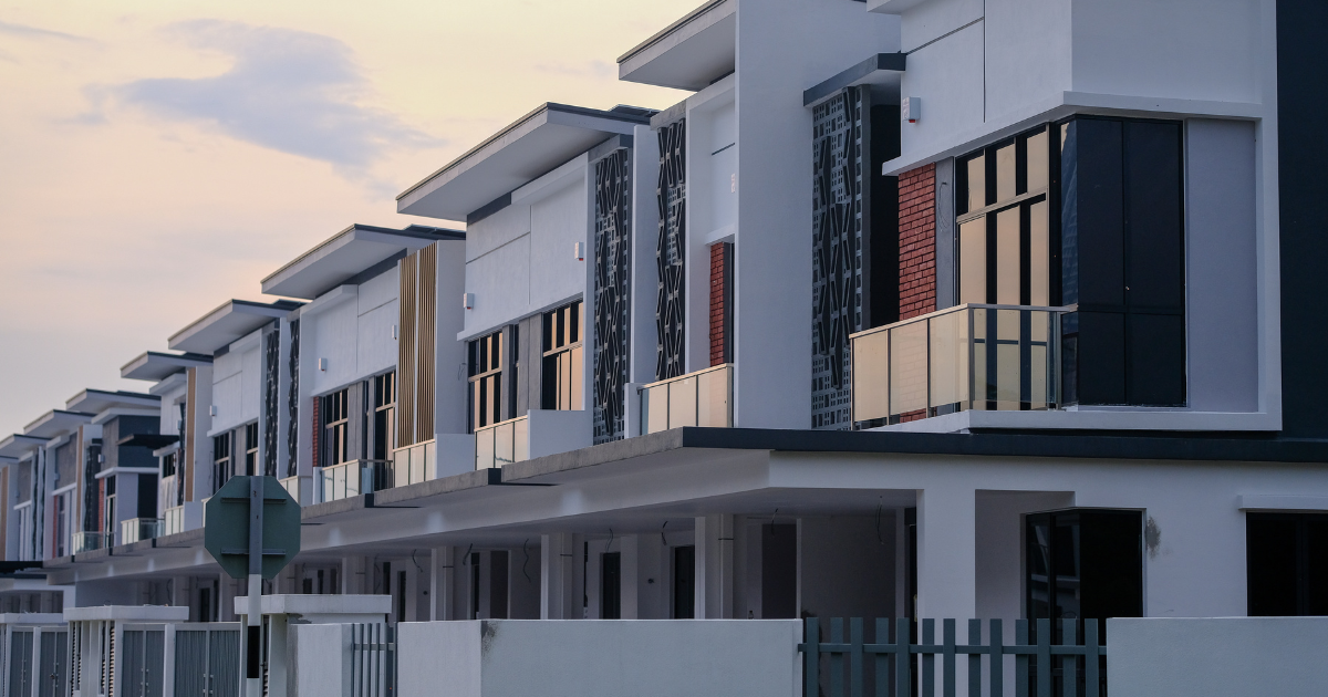 A row of modern terrace houses under construction stands behind a low wall, illustrating shared-wall homes in a gated community